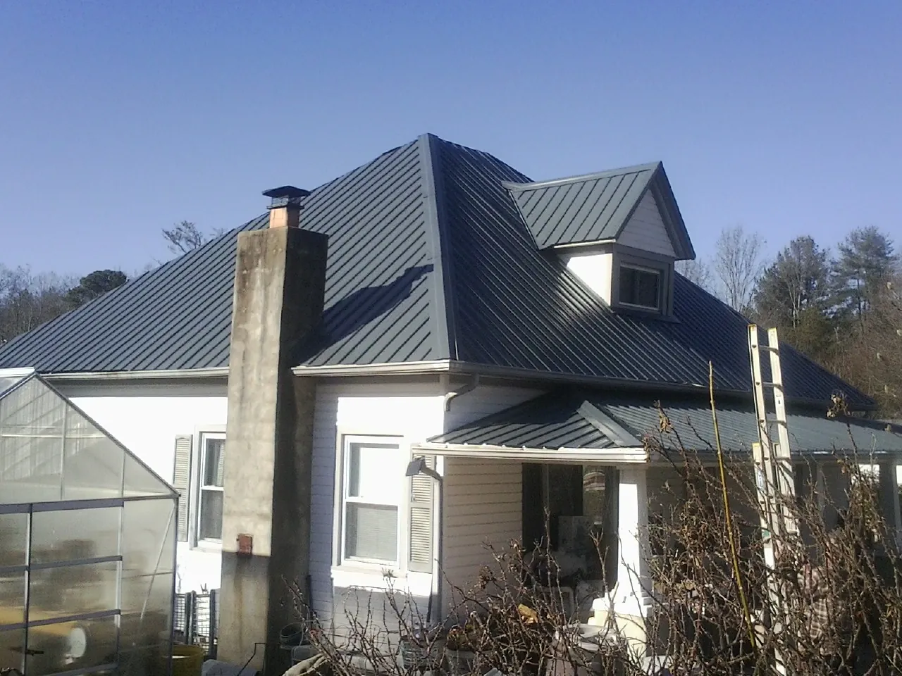 Dark blue standing seam metal roof on a white farmhouse with dormer — Slate & Tile Roof Repair by Roofing Brothers in Alburnett