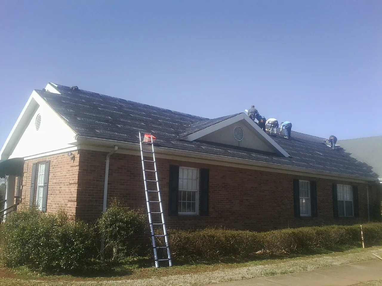 Crew tearing shingles off a brick ranch roof with a ladder set — Emergency Roof Repair work by our crew in Alburnett