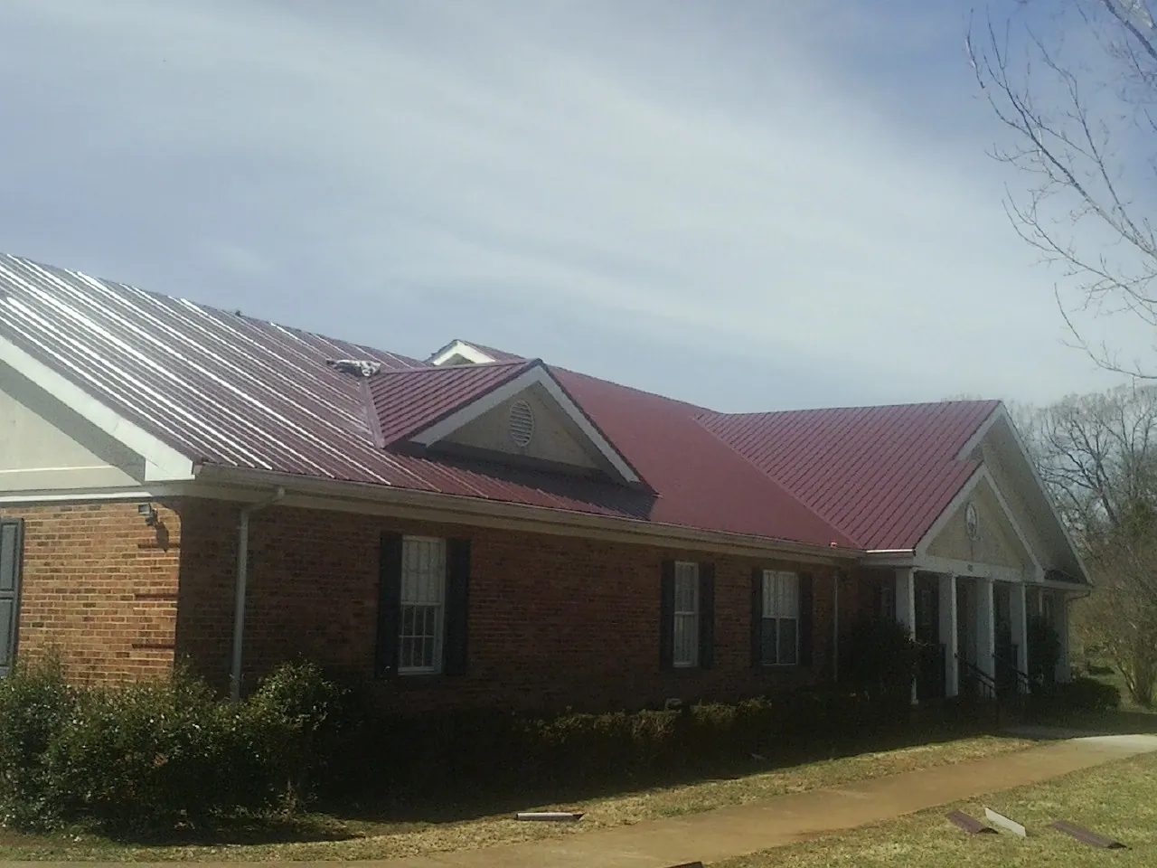 Red metal roof with gabled entries on a long brick building, from a Hail Damage Roof Repair job in Alburnett