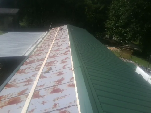 Old rusted panels beside newly installed green metal roofing — Wind Damage Roof Repair by Roofing Brothers in Alburnett