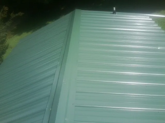 New green metal panels meeting at the ridge of a roof — Flat Roof Repair work by our crew in Alburnett