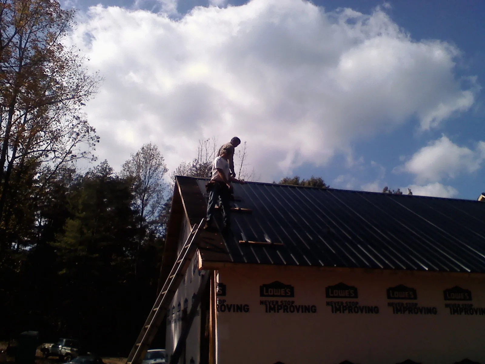 Roofer fastening dark metal panels high against a cloudy sky, from a Roof Inspection job in Alburnett