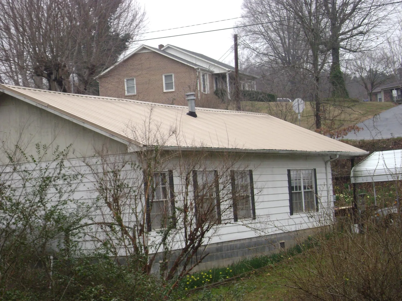 Tan metal roof on a white sided house set into a hillside — Commercial Roofing by Roofing Brothers in Alburnett