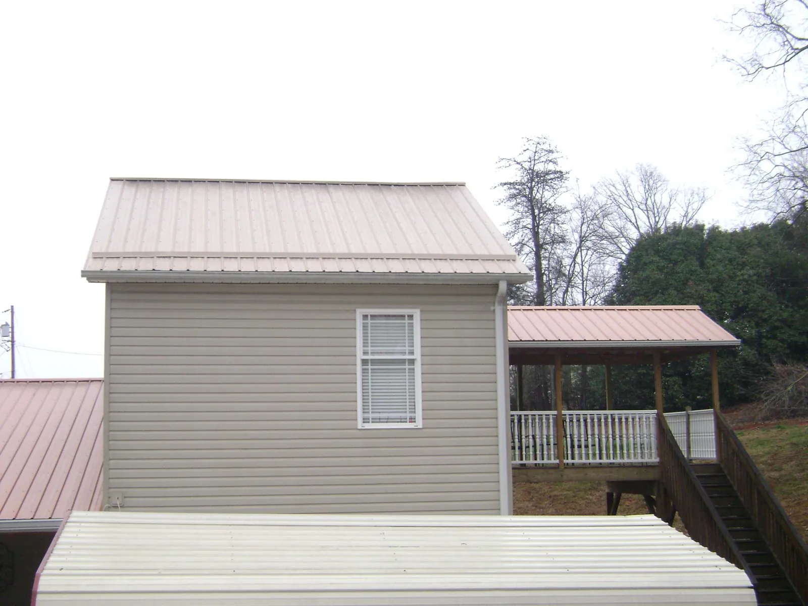 Tan metal roofs on a two story addition and attached porch, from a Roof Replacement job in Alburnett